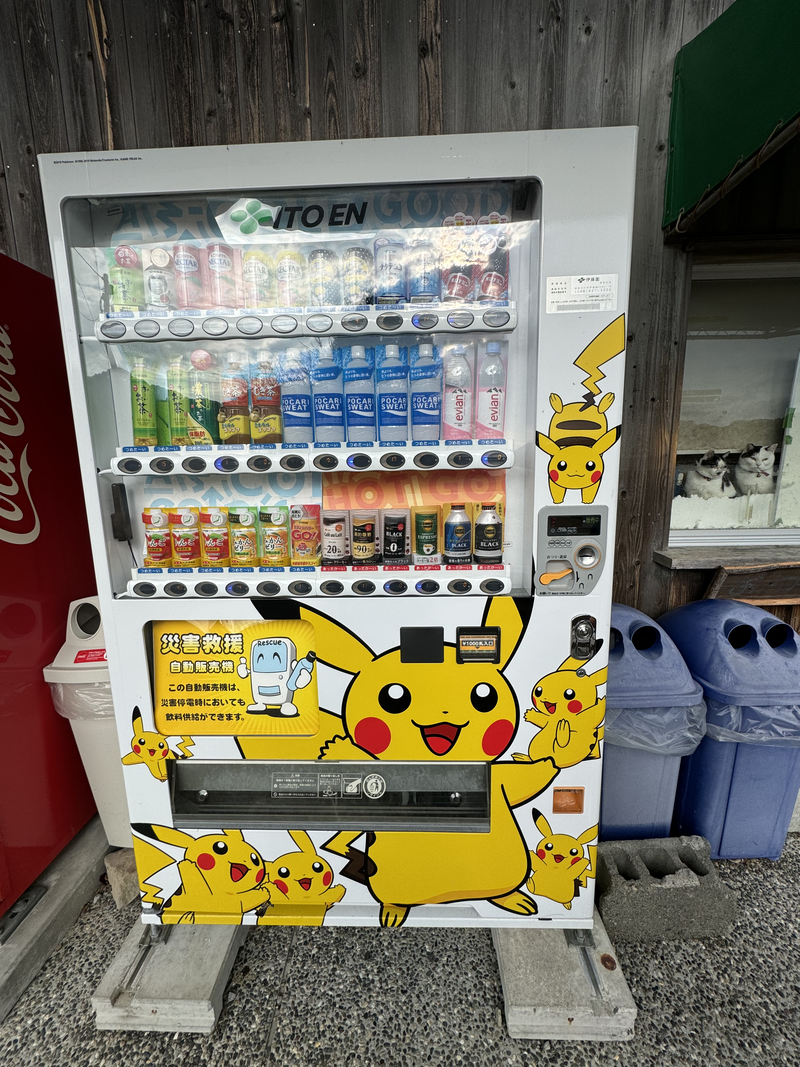 A vending machine emblazoned with Pikachu, and two cats in the window beside